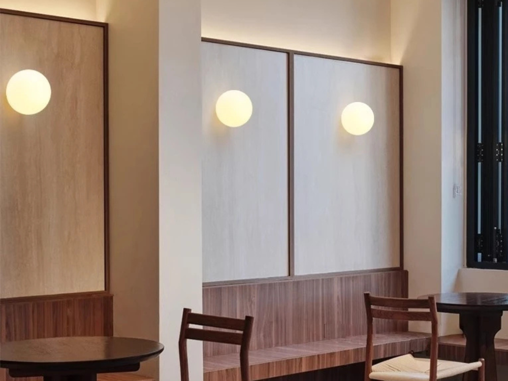Three lit frosted glass globe wall sconces at different heights above a wooden bench