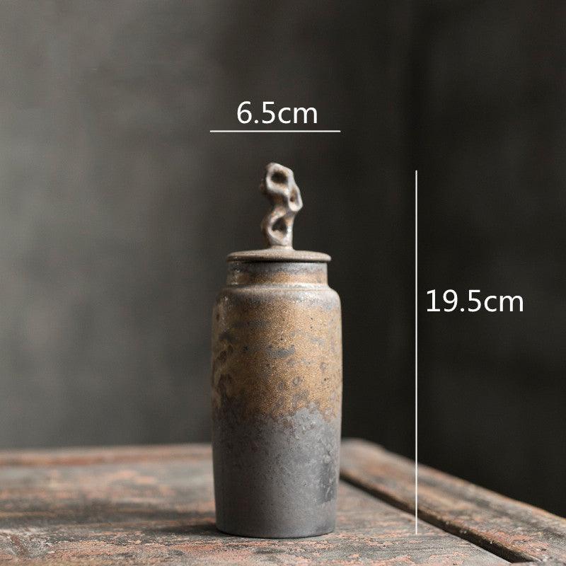 Handmade stoneware tea caddy with airtight ceramic lid on an open shelf beside ceramic tableware