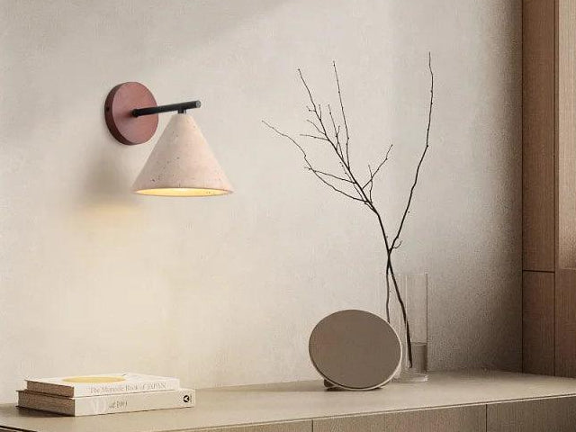 Travertine cone wall sconce on a wood wall plate above a desk with books and a vase
