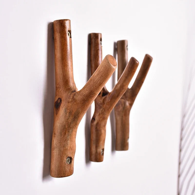Three solid wood branch hooks side by side on a white wall